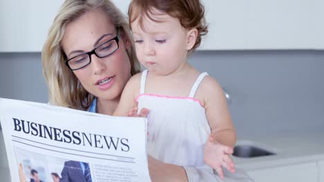 Blonde-mother-reading-newspaper-with-her-baby-at-hone