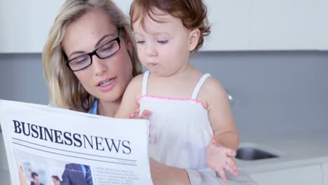 blonde mother reading newspaper with her baby at hone