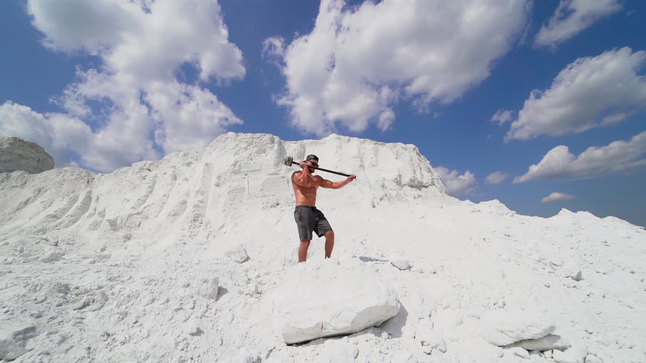 Muscular man on the background of white mountain. Shirtless guy with iron hammer on the natural background of large mountain in summer.