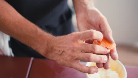 a professional chef combines a rice ball with a piece of salmon and presses them together, making salmon nigiri, traditional japanese cuisine