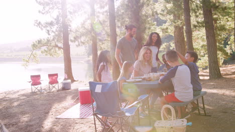 family enjoys picnic as they camp by lake with friends