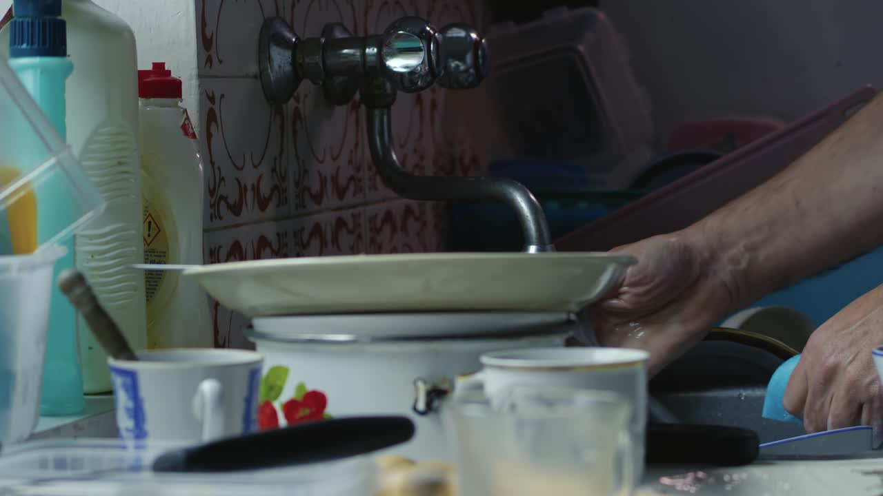 Man Washing up dirty crockery dishes in kitchen sink with soapy sponge