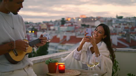 una mujer morena fotografiando una terraza de teléfonos inteligentes. un hombre guapo tocando el ukulele.