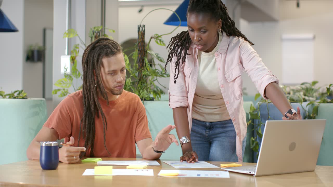 African American team working at table, woman approaching from right, guiding with laptop and notes