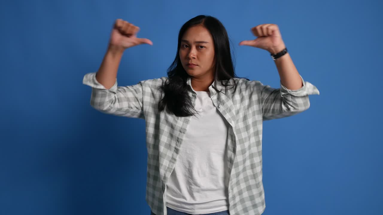 Unhappy young asian woman showing thumbs down isolated on blue background
