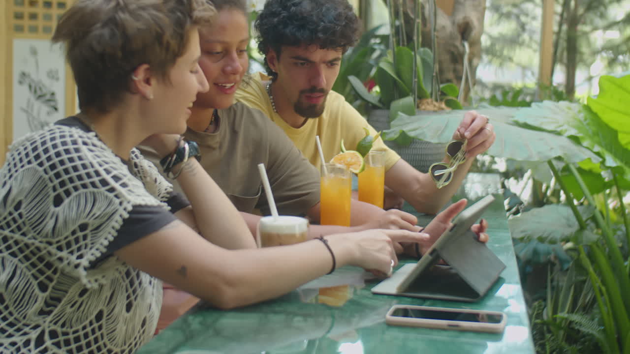 Gen Z Friends Using Tablet and Having Drinks in Outdoor Cafe