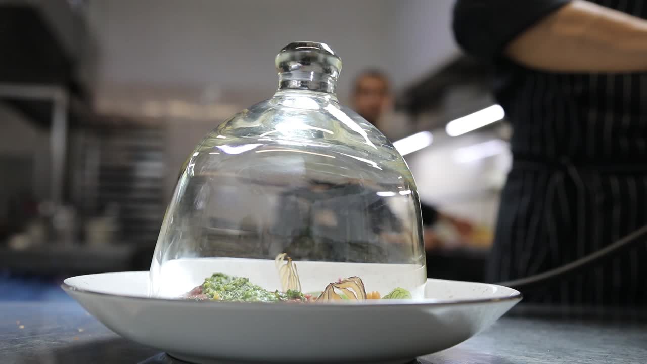 Chef preparing a dish under a glass dome