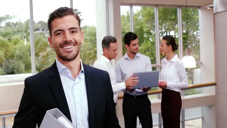 Male-business-executive-smiling-at-camera-while-colleagues-discussing-over-laptop