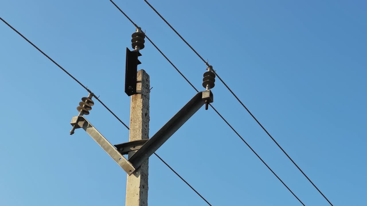 Static shot of an electrical utility pole with insulators and overhead power lines against a clear blue sky, highlighting grid infrastructure, geometry, and linear composition