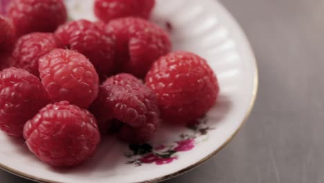 Hand fingers grab raspberry from plate camera slides dolly close-up