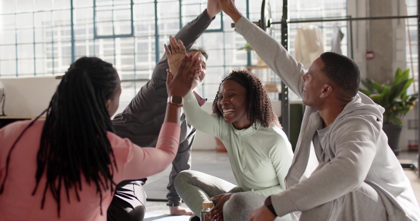 Diverse friends in activewear after class in loft, raising hands and exchanging highfives on mats