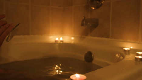 young woman reaches for glass of wine while taking a warm relaxing bath. close up shot on wine glass.