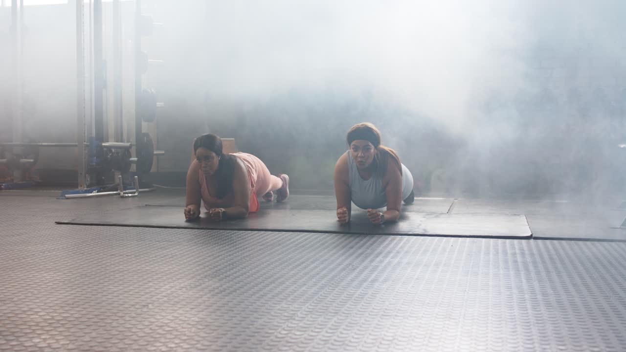 Amiche donne di diverse etnie che si mettono in posizione di plank sugli avambracci su un tappetino in uno studio fitness, rafforzando la forza del core.