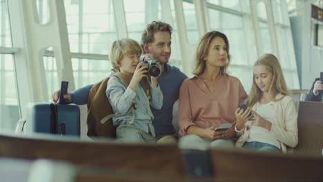 Fröhliche-Familie-Sitzt-In-Der-Abflughalle-Und-Wartet-Auf-Ihren-Flug-Am-Flughafen