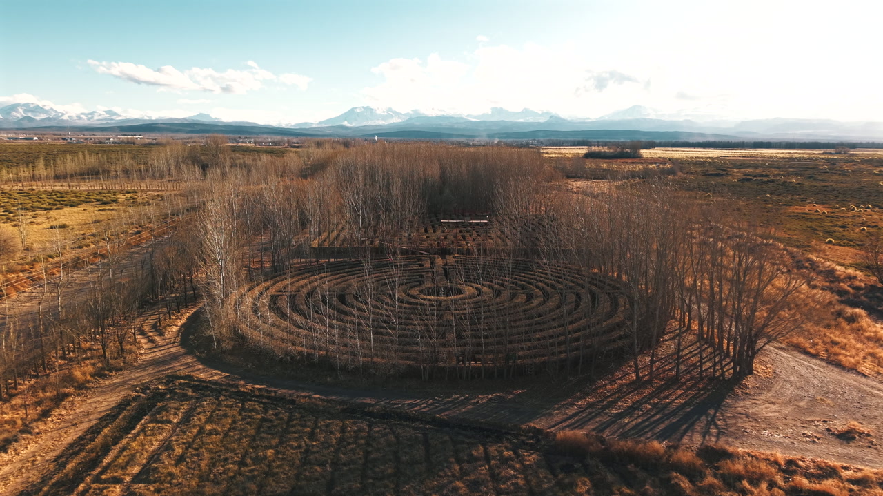 Aerial drone view of a circular hedge maze in dry open countryside with mountains and sky in Argentina.