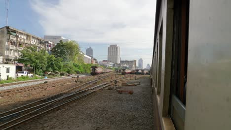 Rail-passenger-view-of-train-leaving-station-with-cityscape-in-background,-Thailand
