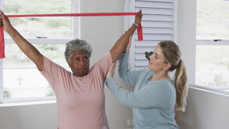 caucasian nurse with senior woman exercising with rubber band, copy space, slow motion