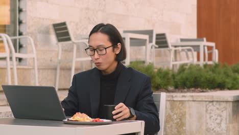Konzentrierter-Geschäftsmann,-Der-Am-Laptop-Arbeitet-Und-Zur-Mittagszeit-In-Einem-Café-Trinkt