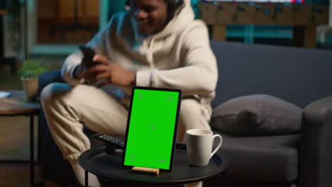 african american young adult laying on the sofa next to mockup copy space, relaxing and browsing web on his smartphone. happy relaxed person on the couch feels happy with remote job. camera a.