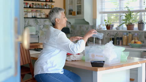 Feliz-Mujer-Birracial-Mayor-Segregando-Residuos-Plásticos-En-Casa,-Cámara-Lenta