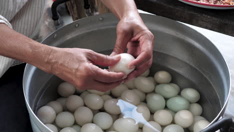 female chef hands peeling duck eggs from big stainless steel pan - food preparation