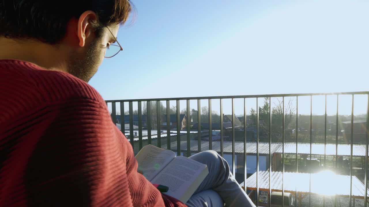 hombre con gafas de lectura leyendo un libro en su balcón bajo el sol y sonándose la nariz
