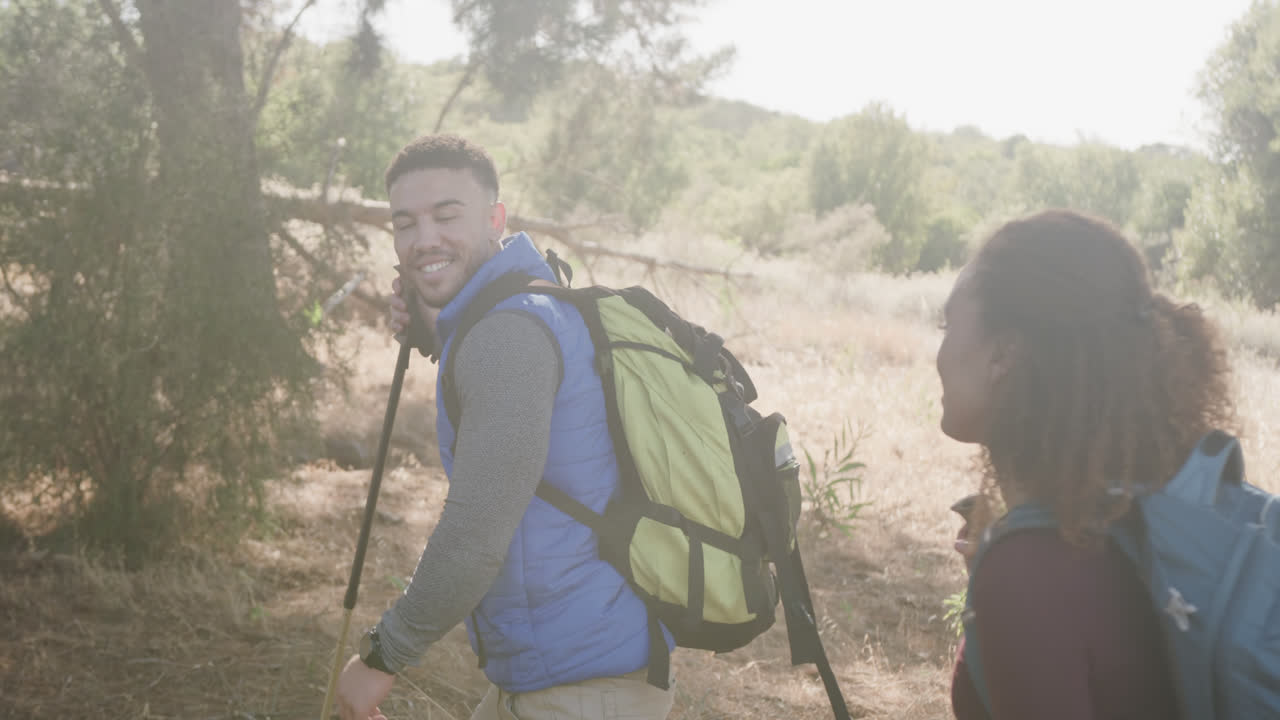 una feliz pareja afroamericana haciendo senderismo con palos de senderismo en el bosque, en cámara lenta