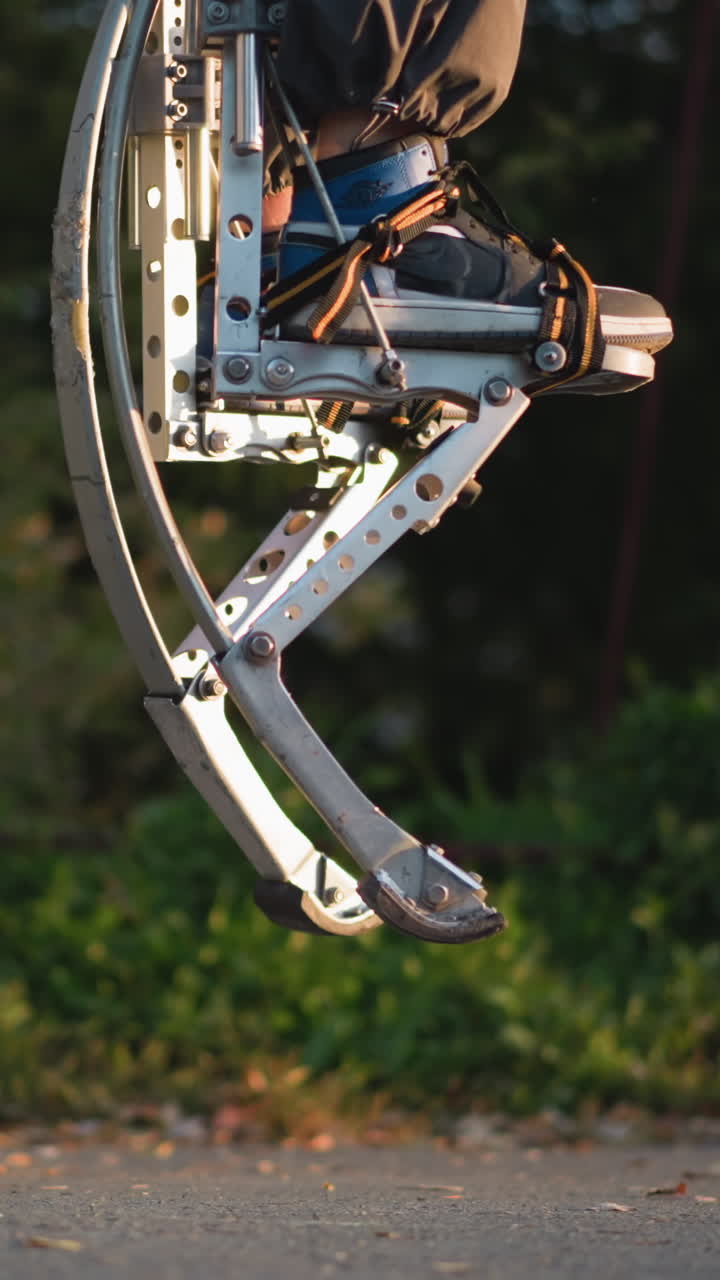 primer plano de piernas con ropa oscura y pilotes de primavera metálicos, saltando en un camino pavimentado. los pilotes muestran un intrincado diseño metálico, y el fondo es un parque verde borroso