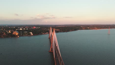 Drone-flight-over-the-San-Roque-González-de-Santa-Cruz-International-Bridge-at-sunset,-while-some-cars-cross-the-border