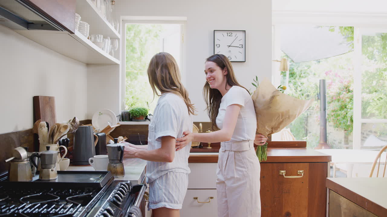 Donna che dà un mazzo di fiori al suo partner gay in cucina a casa.