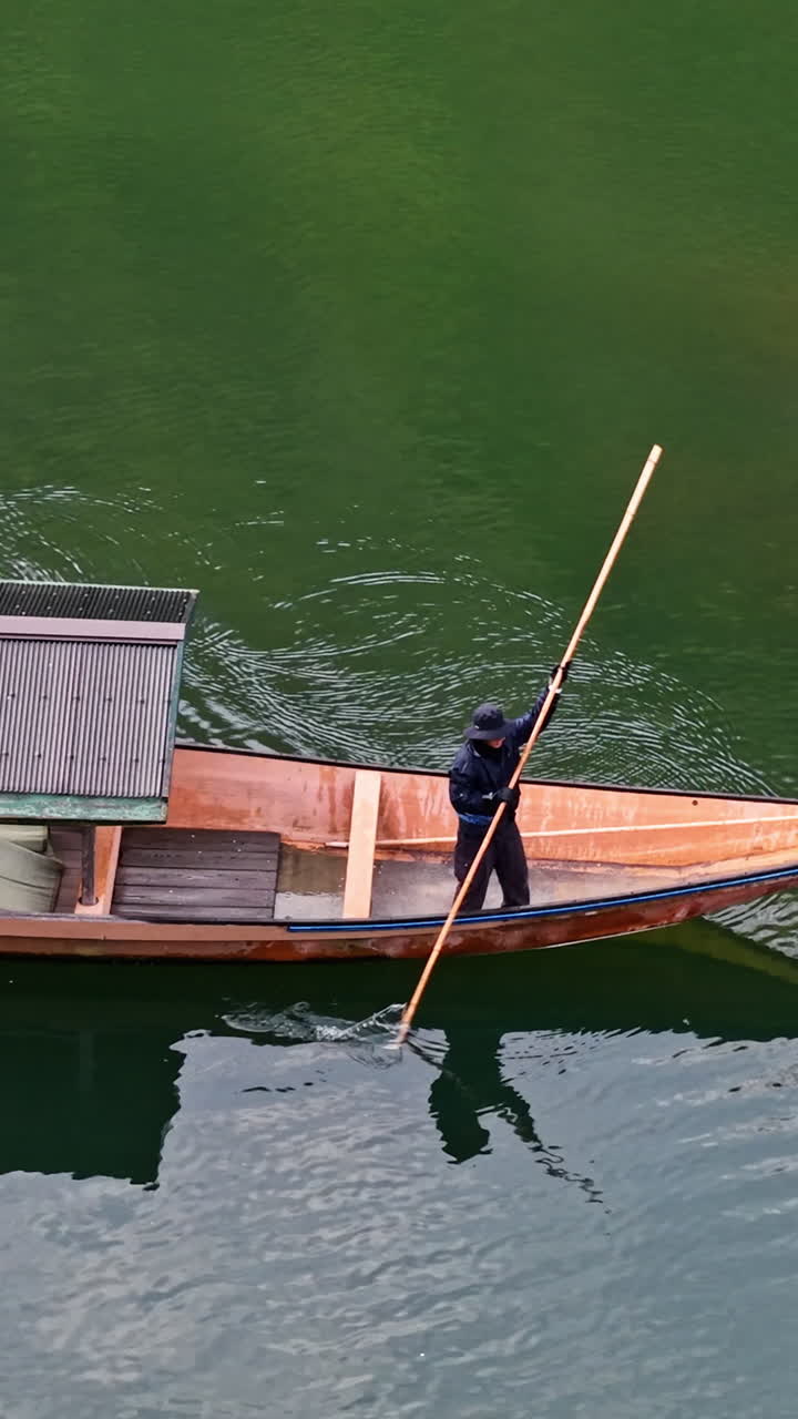 Aerial drone view of a man on a moving boat on the Katsura River in daylight in Arashiyama, Japan