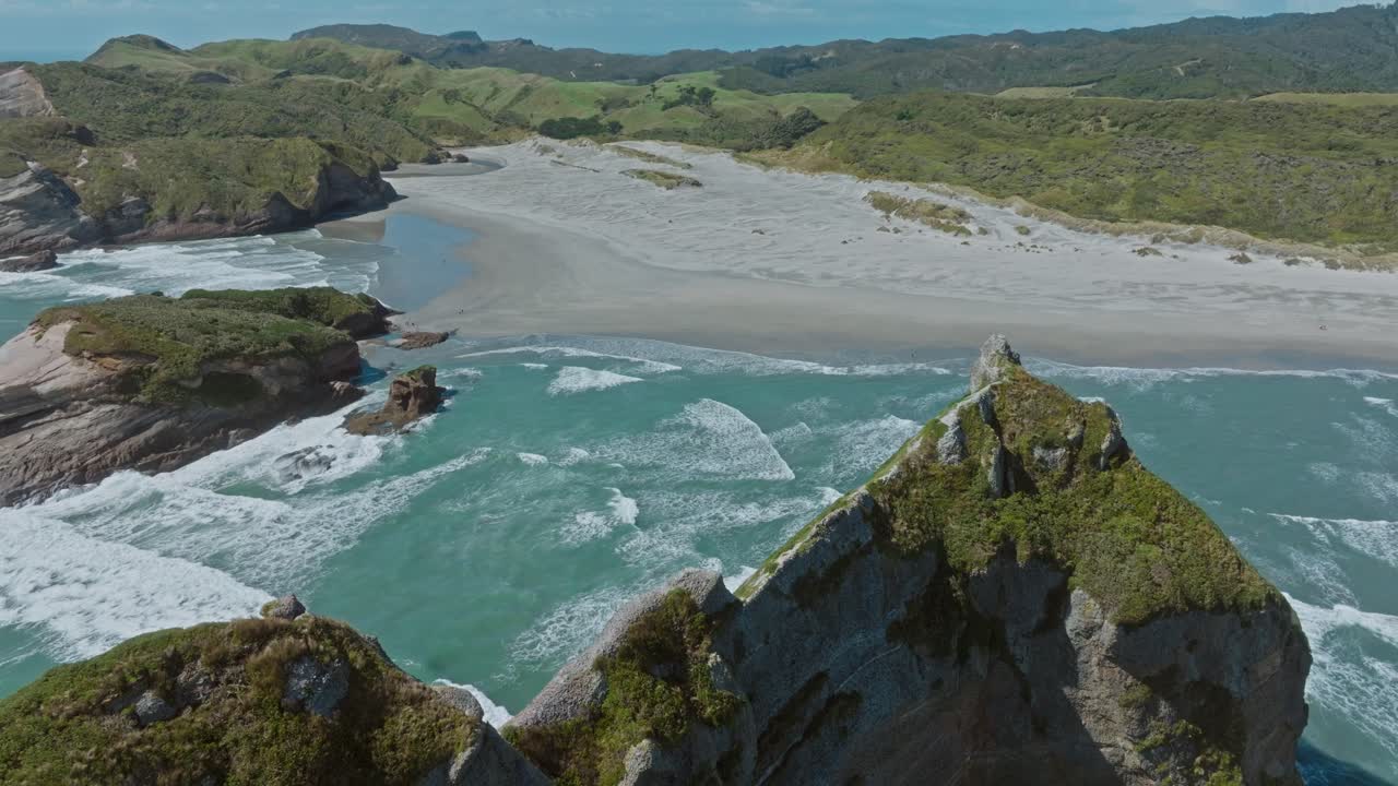 vuelo aéreo inverso con vistas a la pintoresca playa de wharariki y el escarpado paisaje rocoso con cuevas en el mar de tasmania en el cabo de despedida, isla sur de nueva zelanda aotearoa