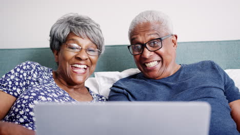 Senior-Couple-Lying-In-Bed-Having-Video-Call-With-Relatives