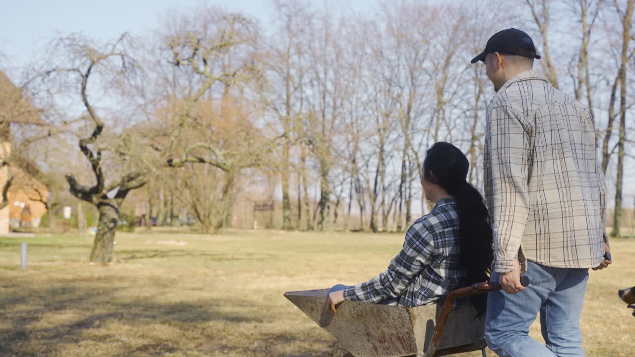 백인 남자가 시골에서  ⁇ 바구니에 그의 파트너를 운반하는 뒷 모습. 그들의 개는 그들을 둘러싸고  ⁇ 는다