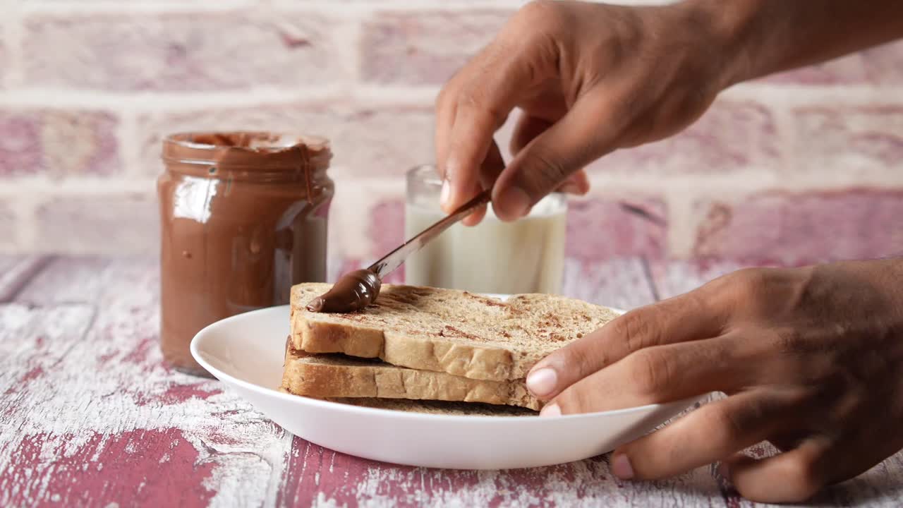 Personne étalant de la pâte à tartiner chocolat-noisette sur du pain grillé