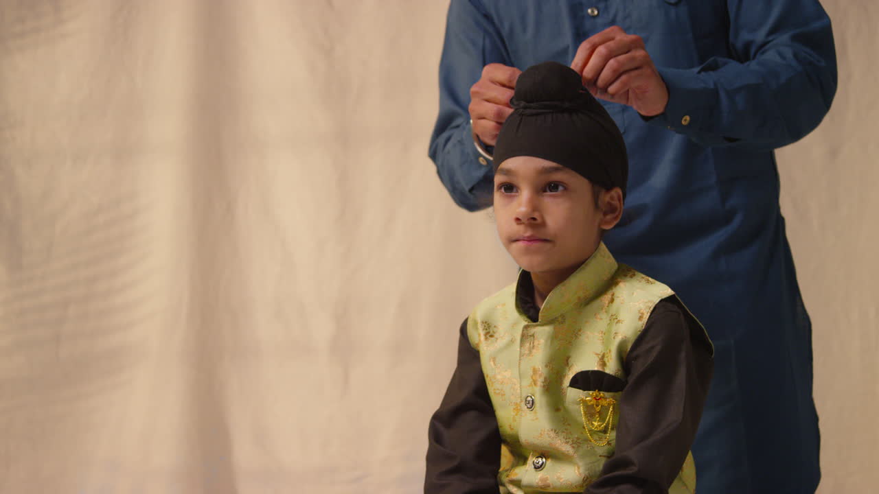 fotografía de estudio de un padre atando un turbante a la cabeza de un joven sikh que lleva un chaleco tradicional como secuencia parte 7 de 10