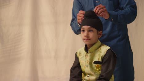 Foto-De-Estudio-De-Un-Padre-Atando-Un-Turbante-En-La-Cabeza-De-Su-Hijo-Sikh-Que-Lleva-Un-Chaleco-Tradicional,-Como-Se-Muestra-En-La-Secuencia,-Parte-7-De-10