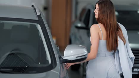 Beautiful-elegant-woman-in-a-suit-approaches-the-car-in-the-showroom-and-straightens-her-lips