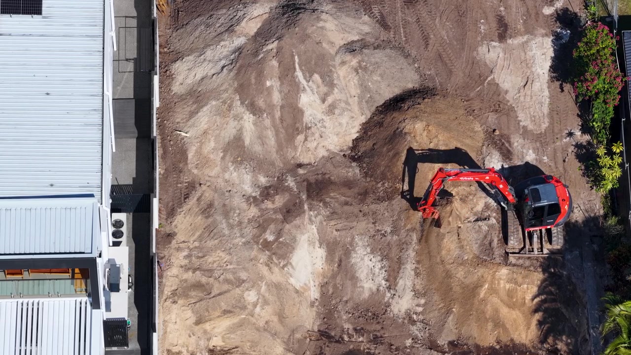 Droneoptagelse ovenfra af en rød gravemaskine, der flytter sand på en byggeplads til boliger