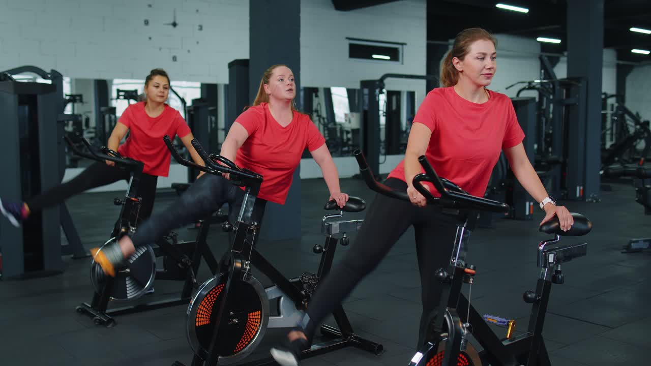 운동 여성 그룹은 실내 체육관에서 스피닝 정지 자전거 루틴에 스트레칭 훈련을합니다.