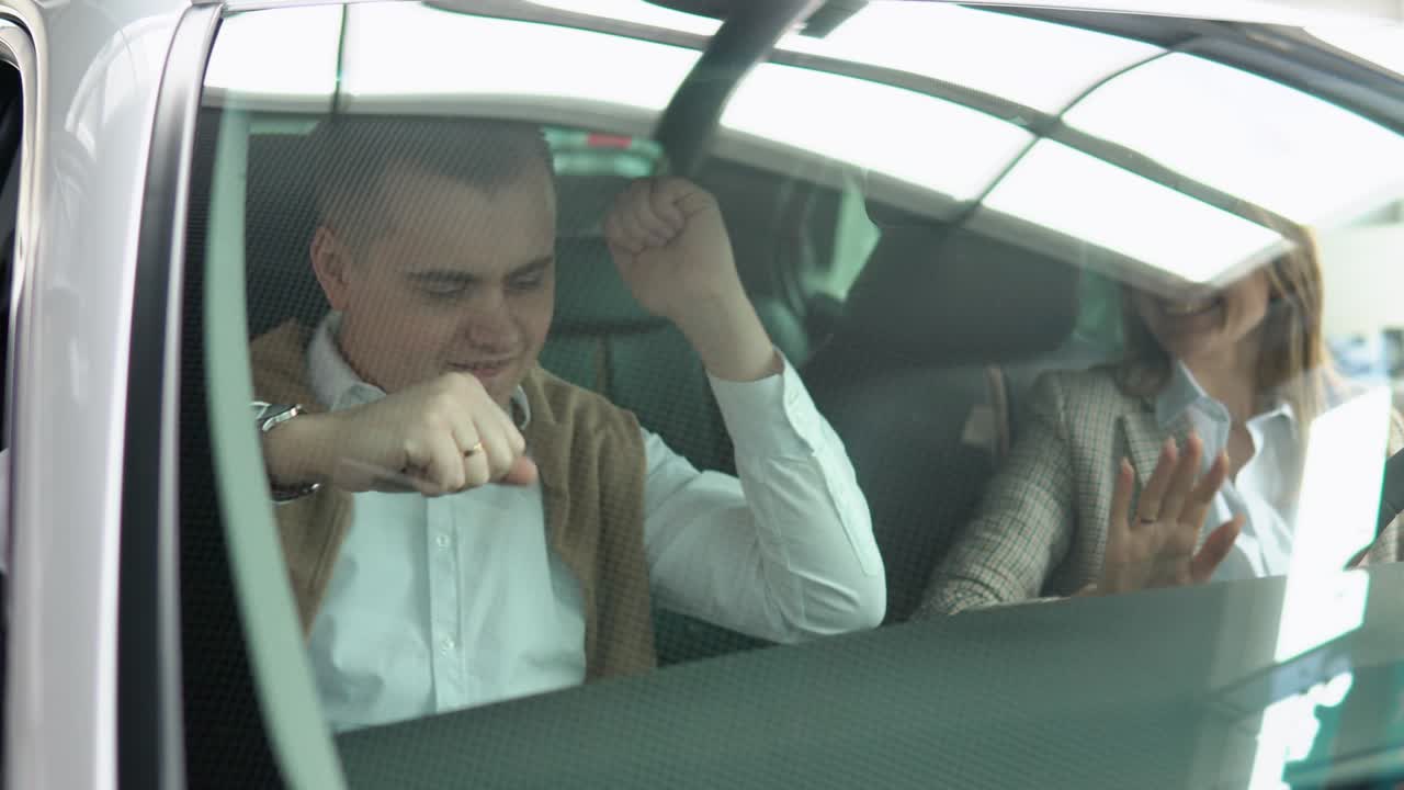Happy couple rejoices in buying a new car. Man and woman smiles and dances in a new car at a car dealership