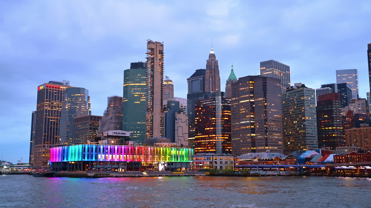 Colorful night view of Lower Manhattan skyline. Skyscrapers of Lower Manhattan glow with lights and colors along the waterfront