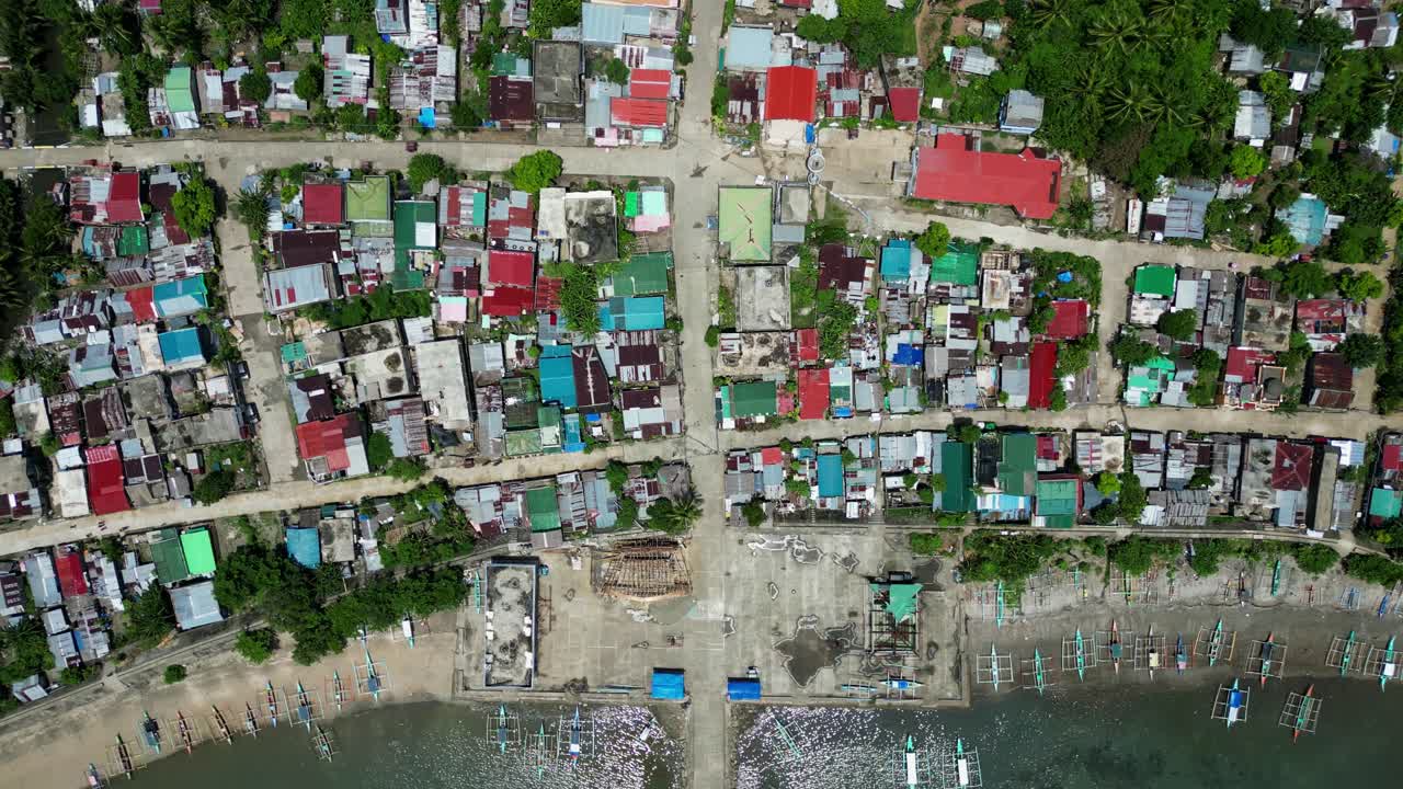 Bird’s eye Aerial view of Colorful, coastal village and rooftops with fishing boats docked along idyllic shoreline in Catanduanes, Philippines