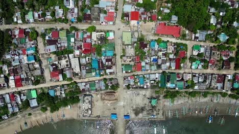 bird’s eye aerial view of colorful, coastal village and rooftops with fishing boats docked along idyllic shoreline in catanduanes, philippines