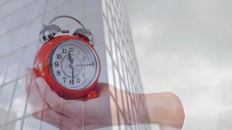 holding red alarm clock, hand animation over building and sky background