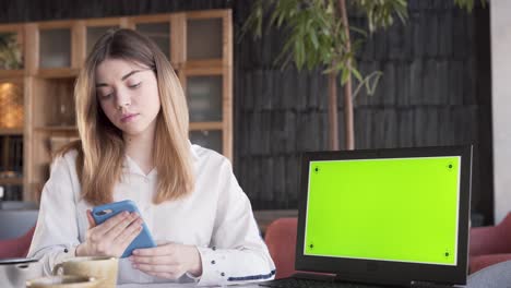 una joven encantadora está sentada cerca de la laptop mostrando una pantalla verde