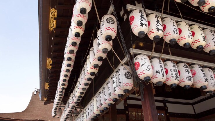 Inquadratura dal basso di lanterne di carta bianche con calligrafia rossa sotto le grondaie di un tempio a Kyoto.
