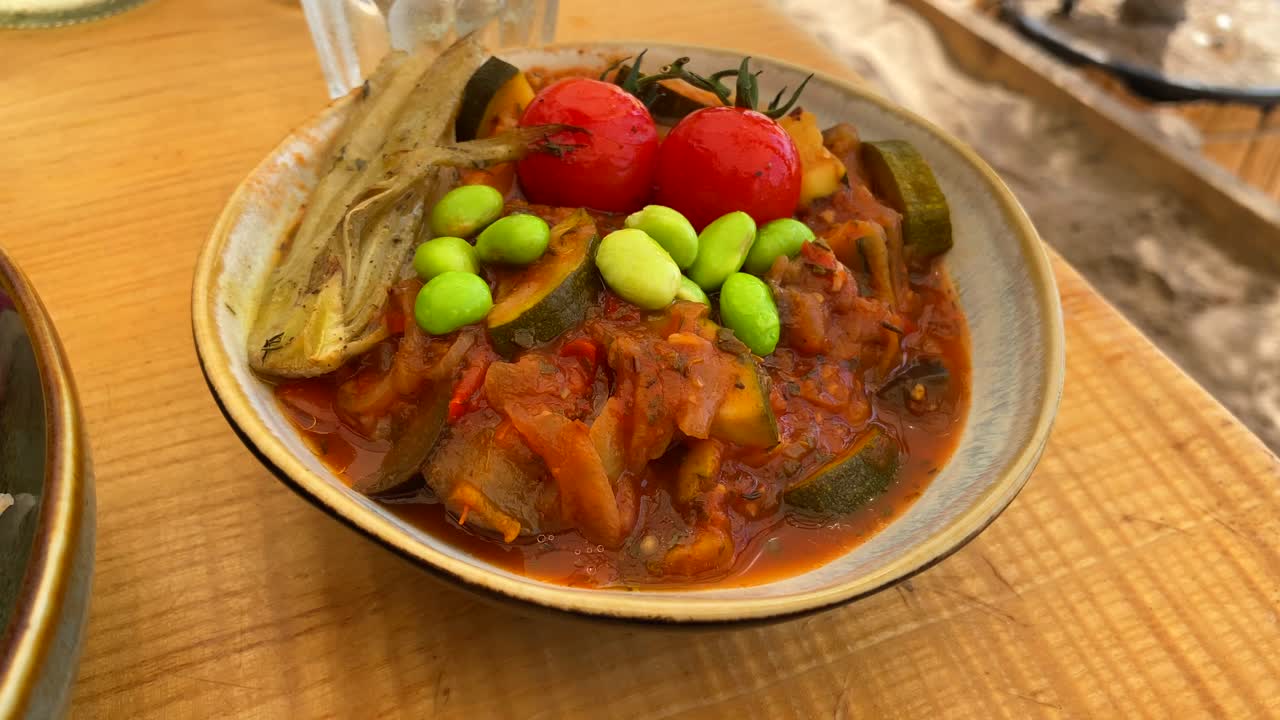 sabroso plato de ratatouille francés con verduras estofadas, tomates cereza y frijoles edamame japoneses en un cuenco, tiro de 4k