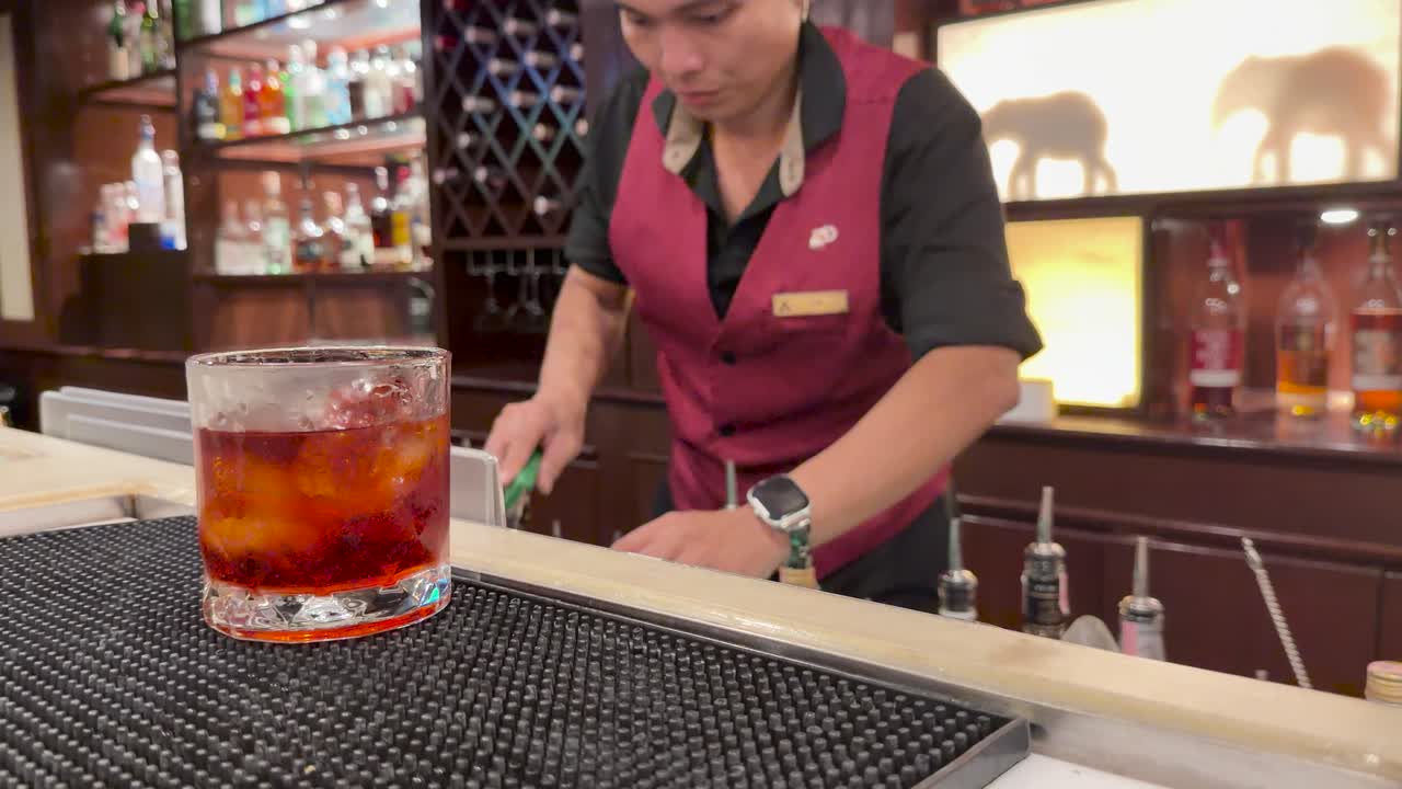 Bartender prepares and garnishes Negroni cocktail in elegant bar with warm, ambient lighting