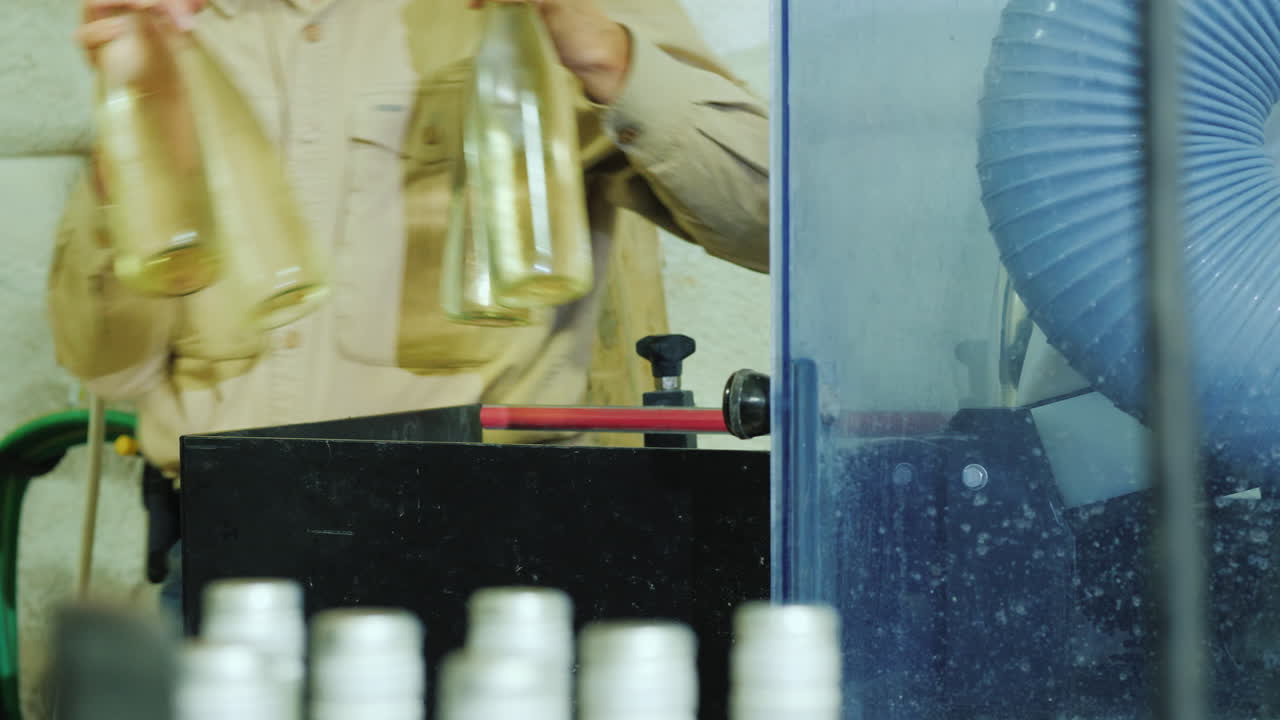 작업자가 작은 와이너리에서 일하는 컨베이어 벨트에서 와인병을 집어들고 있습니다.